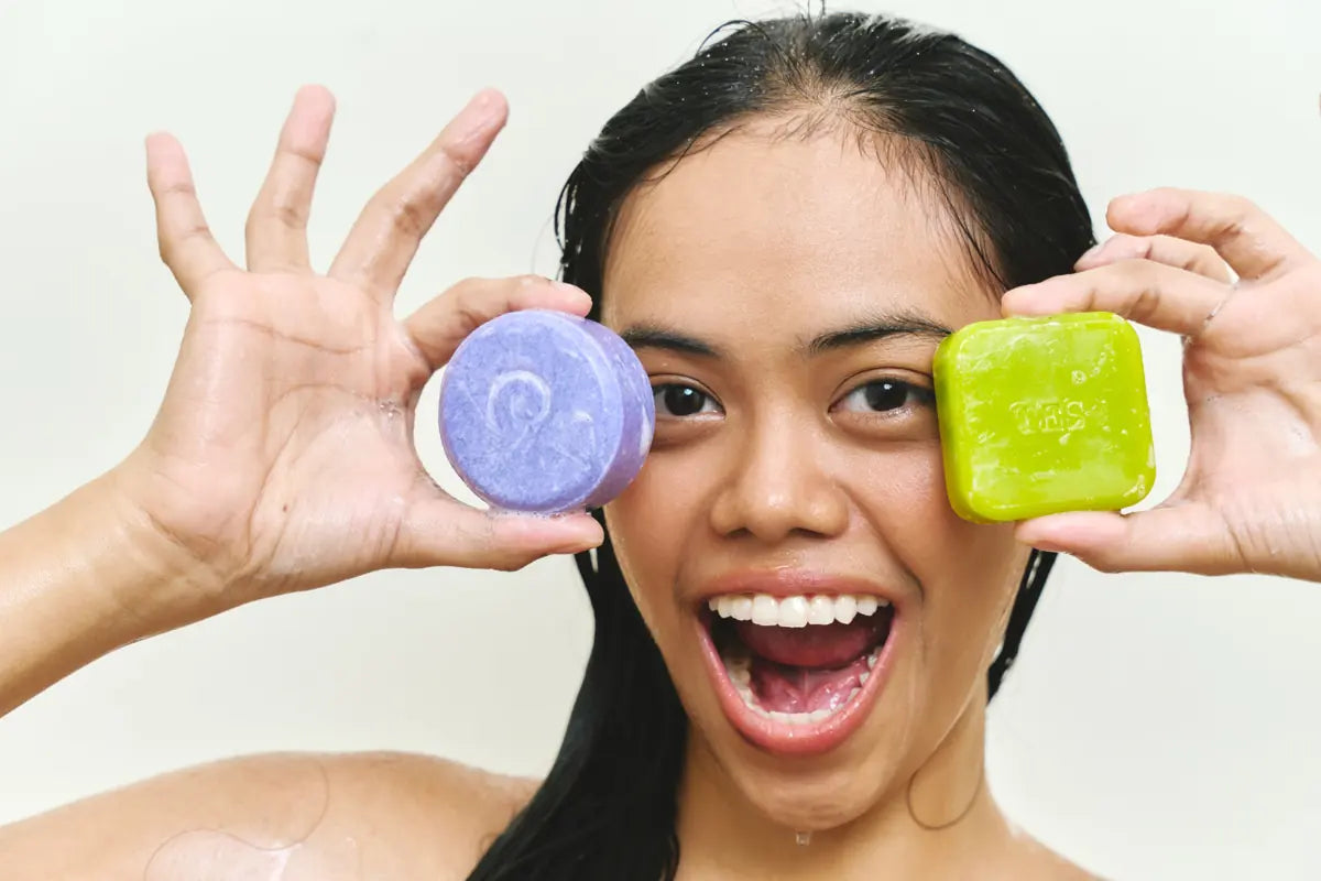 Excited woman holding a purple shampoo bar and a green soap bar