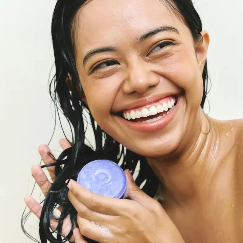 Woman laughing while washing her hair with a purple shampoo bar